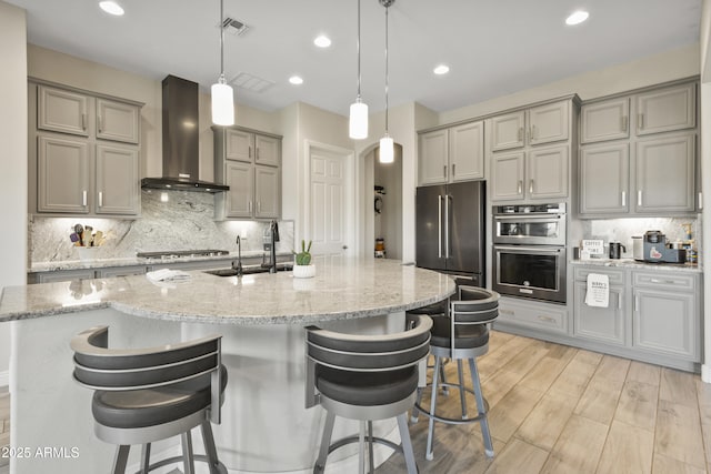 kitchen featuring visible vents, backsplash, gray cabinetry, appliances with stainless steel finishes, and wall chimney range hood