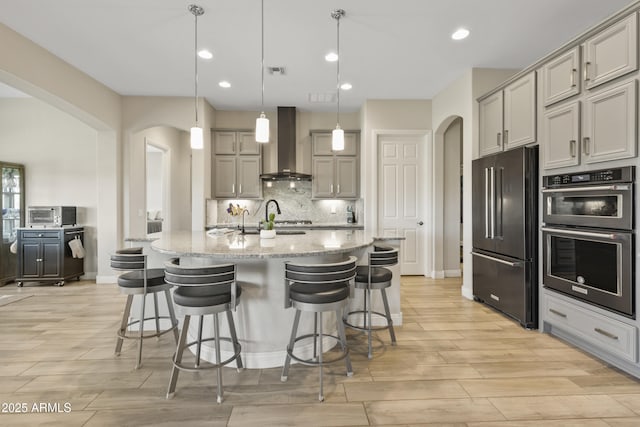 kitchen with double wall oven, wall chimney range hood, high end refrigerator, and arched walkways