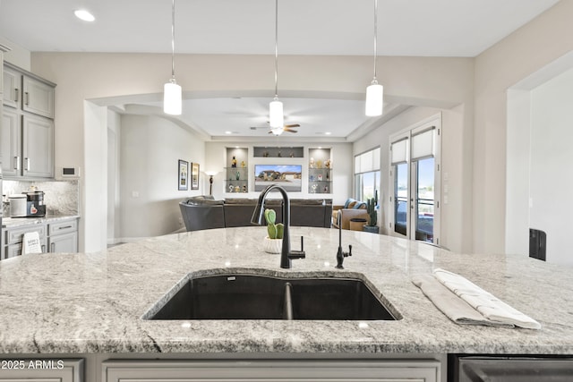 kitchen featuring hanging light fixtures, light stone counters, open floor plan, and a sink