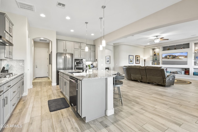 kitchen with arched walkways, gray cabinetry, visible vents, open floor plan, and a kitchen bar