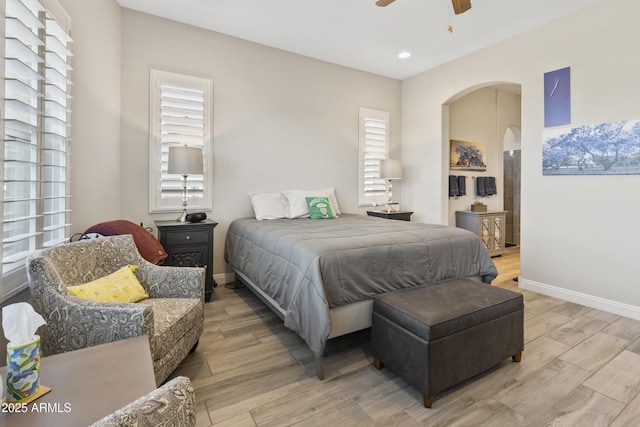 bedroom featuring arched walkways, baseboards, multiple windows, and light wood finished floors