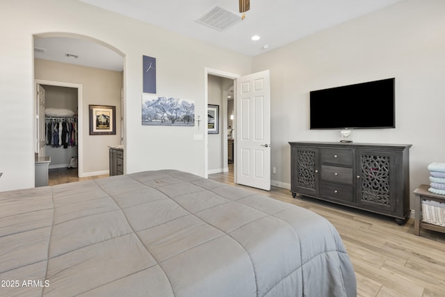 bedroom with arched walkways, visible vents, baseboards, light wood-style floors, and a spacious closet