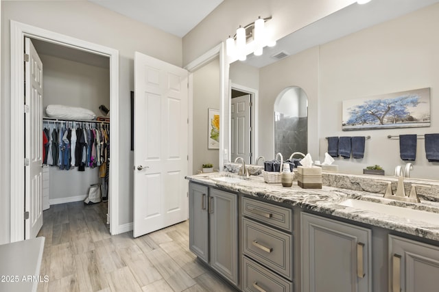 bathroom featuring double vanity, visible vents, tiled shower, wood finished floors, and a sink