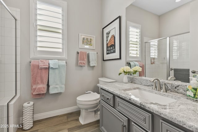 bathroom featuring toilet, wood finished floors, vanity, baseboards, and a stall shower