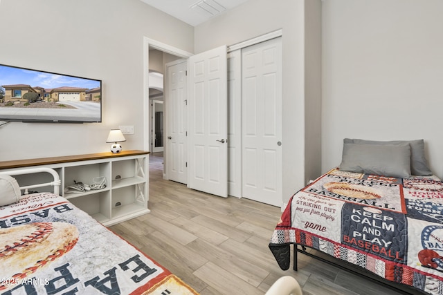 bedroom with light wood finished floors, visible vents, arched walkways, and a closet