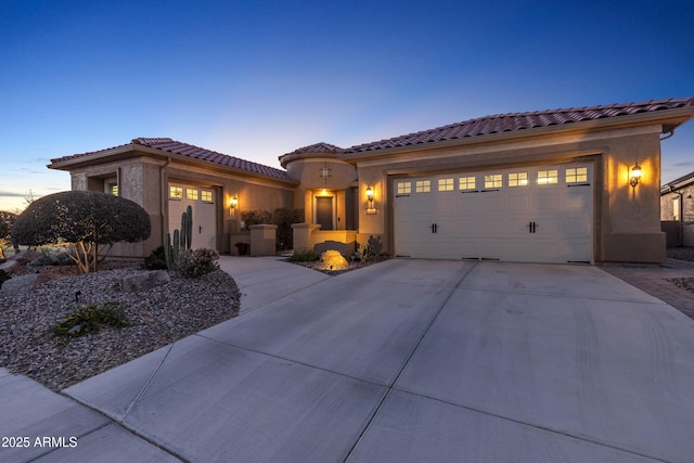 mediterranean / spanish-style house with a garage, concrete driveway, a tiled roof, and stucco siding