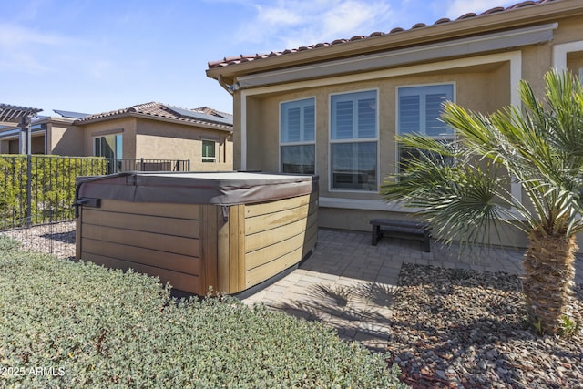 view of side of property featuring a hot tub, fence, a patio, and stucco siding