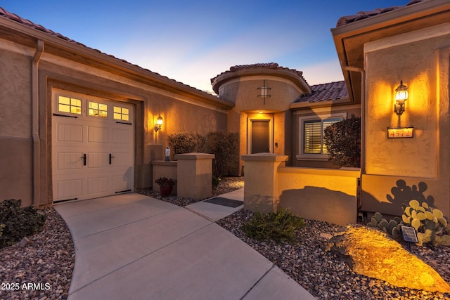 property entrance with a garage, concrete driveway, a tiled roof, and stucco siding