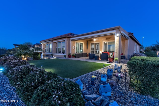 rear view of property featuring a patio, a lawn, and stucco siding