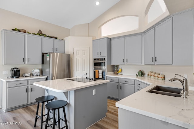 kitchen featuring a kitchen island, light stone countertops, appliances with stainless steel finishes, and sink