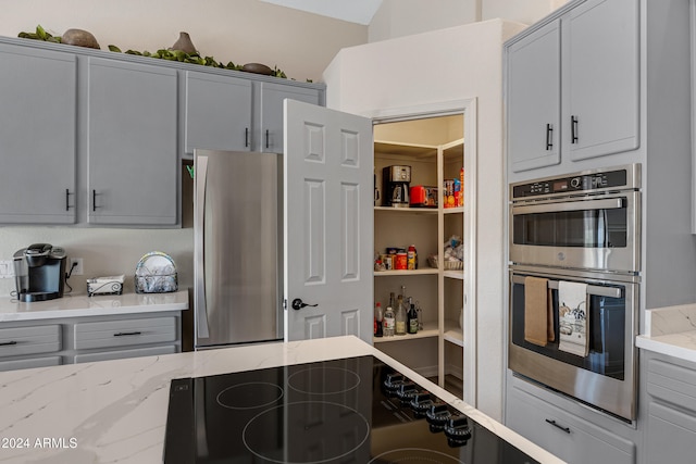 kitchen with light stone countertops, gray cabinetry, and appliances with stainless steel finishes