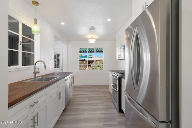 kitchen with sink, wood counters, pendant lighting, white cabinets, and appliances with stainless steel finishes