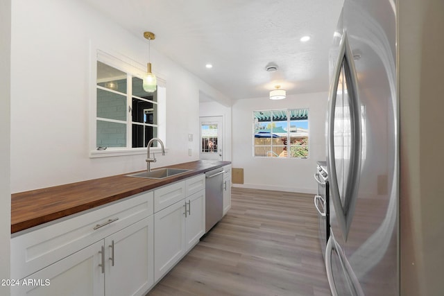 kitchen featuring white cabinetry, sink, hanging light fixtures, butcher block countertops, and appliances with stainless steel finishes