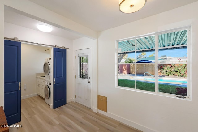 clothes washing area with a barn door, cabinets, light hardwood / wood-style floors, and stacked washer / drying machine