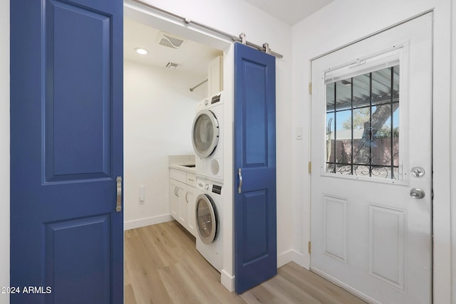 laundry area featuring cabinets, light wood-type flooring, a barn door, and stacked washer / drying machine