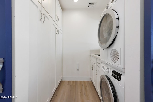 washroom with cabinets, light hardwood / wood-style flooring, and stacked washer and clothes dryer