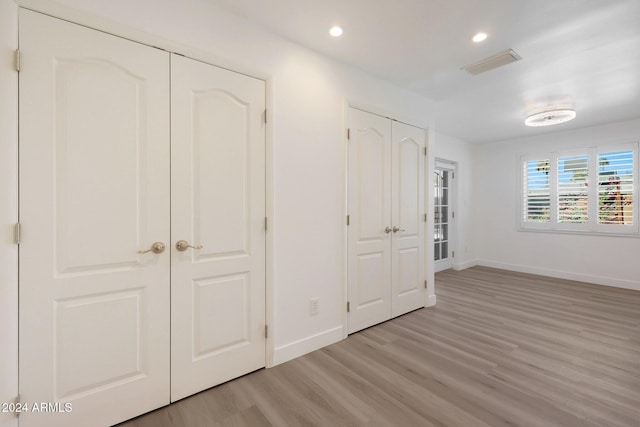 unfurnished bedroom with two closets and light wood-type flooring