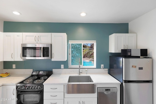 kitchen with white cabinets, appliances with stainless steel finishes, light stone counters, and sink