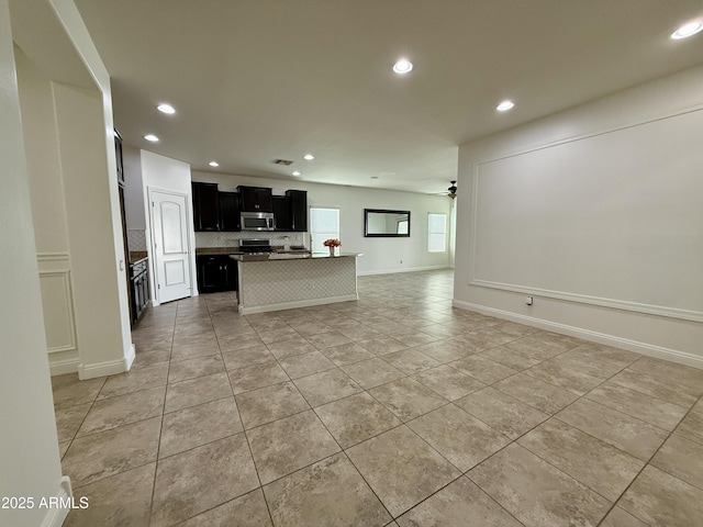 kitchen with a kitchen island with sink, appliances with stainless steel finishes, ceiling fan, light tile patterned flooring, and tasteful backsplash