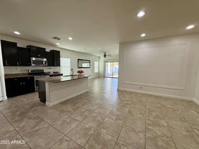 kitchen featuring stainless steel appliances, an island with sink, light tile patterned floors, ceiling fan, and sink