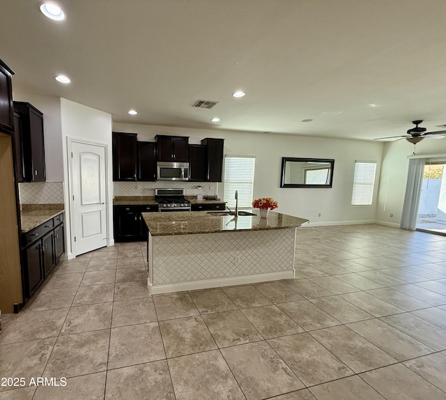 kitchen with dark stone countertops, stainless steel appliances, an island with sink, sink, and light tile patterned flooring