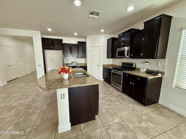 kitchen with light stone countertops, light tile patterned floors, a kitchen island with sink, appliances with stainless steel finishes, and sink