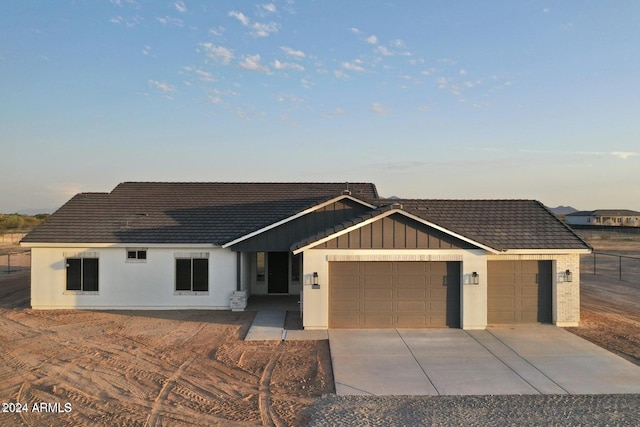 view of front facade with driveway, board and batten siding, an attached garage, and a tiled roof