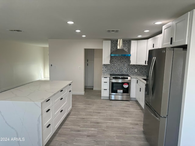 kitchen featuring light stone countertops, wall chimney range hood, white cabinetry, and stainless steel appliances