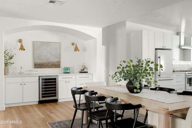 kitchen with white cabinets, light wood-type flooring, white appliances, and wine cooler