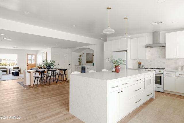 kitchen with a center island, wall chimney range hood, pendant lighting, white appliances, and white cabinets