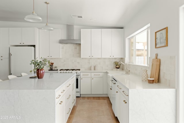 kitchen featuring pendant lighting, white appliances, sink, wall chimney exhaust hood, and white cabinetry