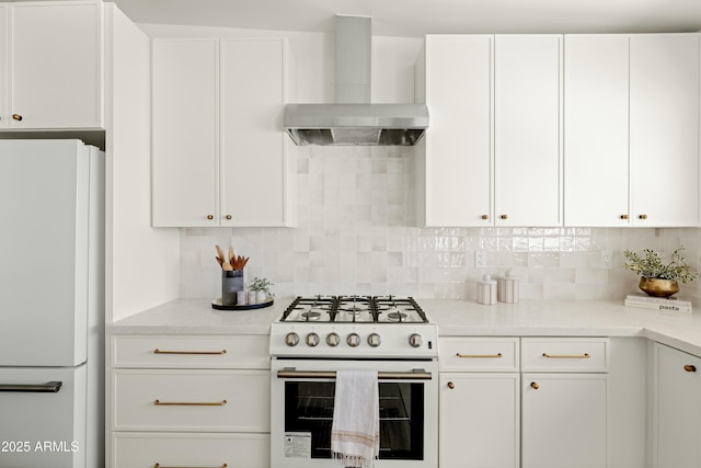 kitchen featuring gas range, white refrigerator, white cabinetry, and wall chimney exhaust hood