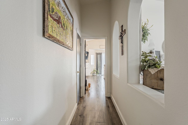 corridor featuring arched walkways, baseboards, and wood finished floors