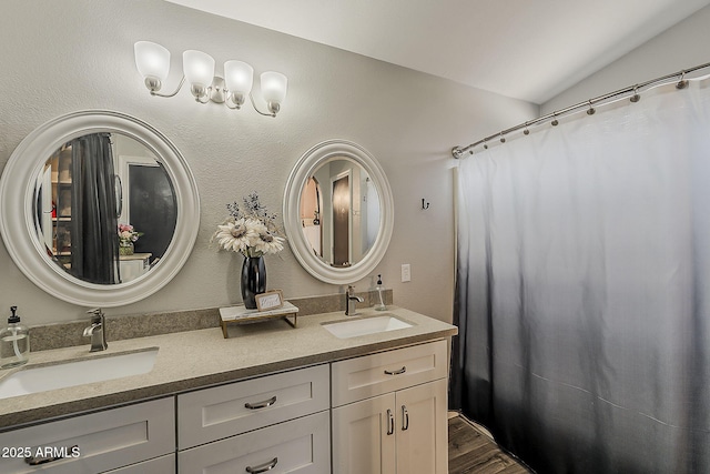 bathroom with a sink, double vanity, vaulted ceiling, and wood finished floors