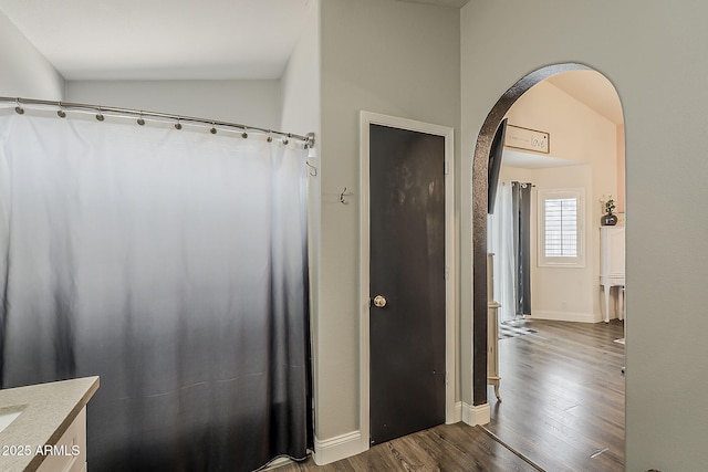 bathroom featuring vanity, lofted ceiling, baseboards, and wood finished floors