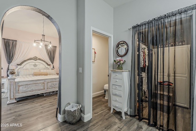 bedroom with baseboards, arched walkways, a chandelier, and wood finished floors