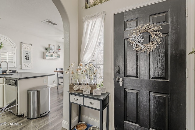 entryway with arched walkways, baseboards, visible vents, and wood finished floors