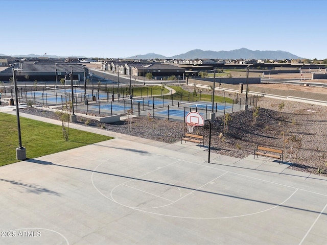 view of property's community with a tennis court, a lawn, fence, a mountain view, and community basketball court