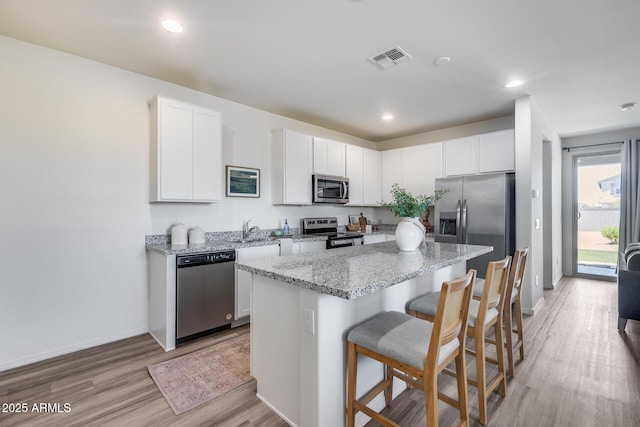17728 W Paraiso Dr, Surprise, AZ 85387 - kitchen featuring appliances with stainless steel finishes, light wood-style floors, a kitchen island, a kitchen breakfast bar, and light stone counters
