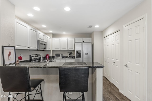 kitchen featuring a breakfast bar area, stainless steel appliances, kitchen peninsula, dark hardwood / wood-style flooring, and white cabinetry