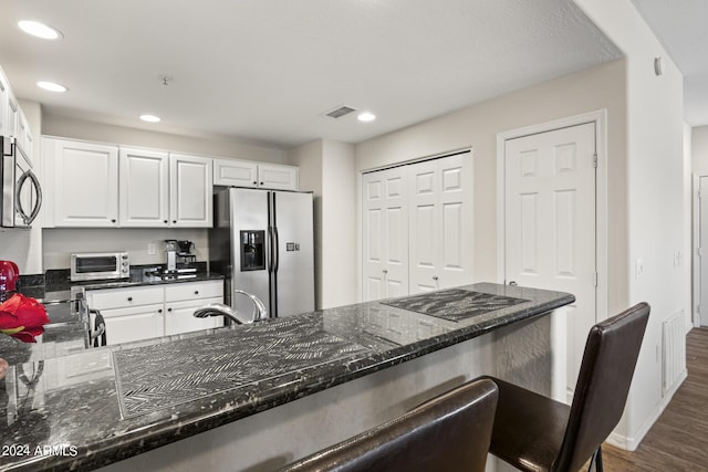 kitchen with sink, white cabinets, dark stone counters, dark hardwood / wood-style flooring, and appliances with stainless steel finishes