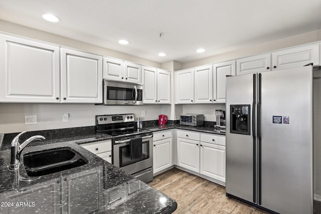 kitchen featuring light wood-type flooring, white cabinetry, appliances with stainless steel finishes, dark stone countertops, and sink