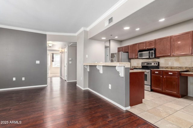 2134 E Broadway Rd Unit 1062, Tempe, AZ 85282 - kitchen featuring stainless steel appliances, a peninsula, a kitchen breakfast bar, light wood-style flooring, and ornamental molding