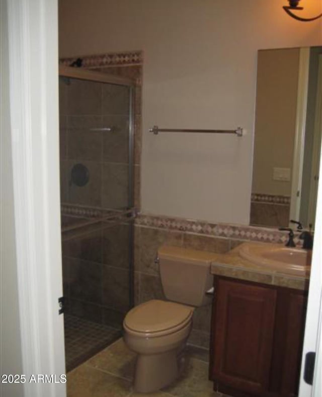 bathroom with toilet, a wainscoted wall, vanity, tile walls, and a tile shower