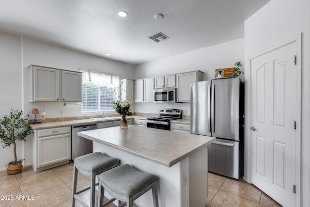 kitchen featuring visible vents, light tile patterned floors, appliances with stainless steel finishes, a kitchen breakfast bar, and a sink