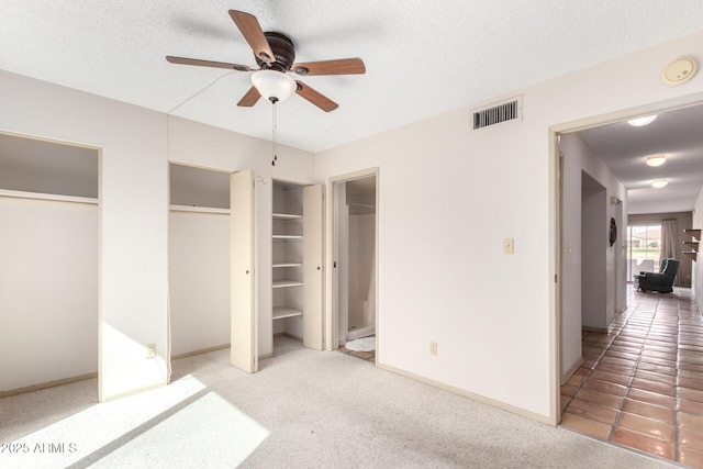 unfurnished bedroom featuring multiple closets, ceiling fan, carpet flooring, and a textured ceiling