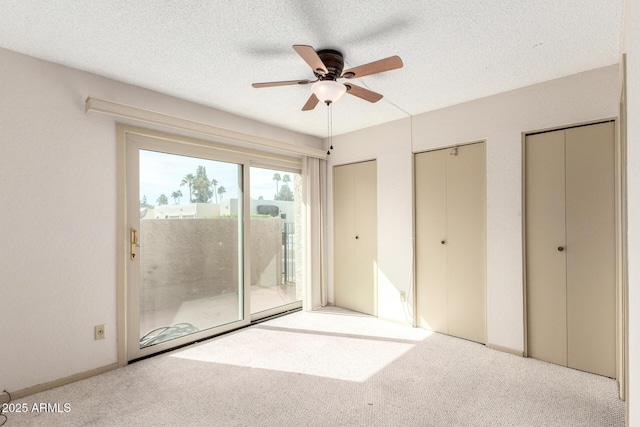 unfurnished bedroom with multiple closets, light colored carpet, access to exterior, and a textured ceiling