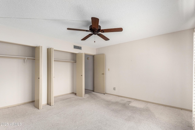 unfurnished bedroom featuring ceiling fan, light carpet, two closets, and a textured ceiling