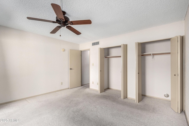 unfurnished bedroom featuring ceiling fan, light colored carpet, a textured ceiling, and two closets