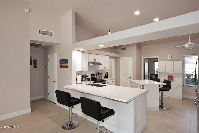 kitchen with visible vents, under cabinet range hood, a breakfast bar area, stainless steel range with electric cooktop, and a peninsula